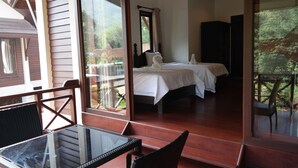 Un dormitorio con dos camas, un ventanal de vidrio que da a un espacio exterior y una mesa con sillas.