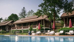 Una piscina con sillones de descanso y sombrillas, rodeada de edificios con fachada de madera y un porche cubierto.