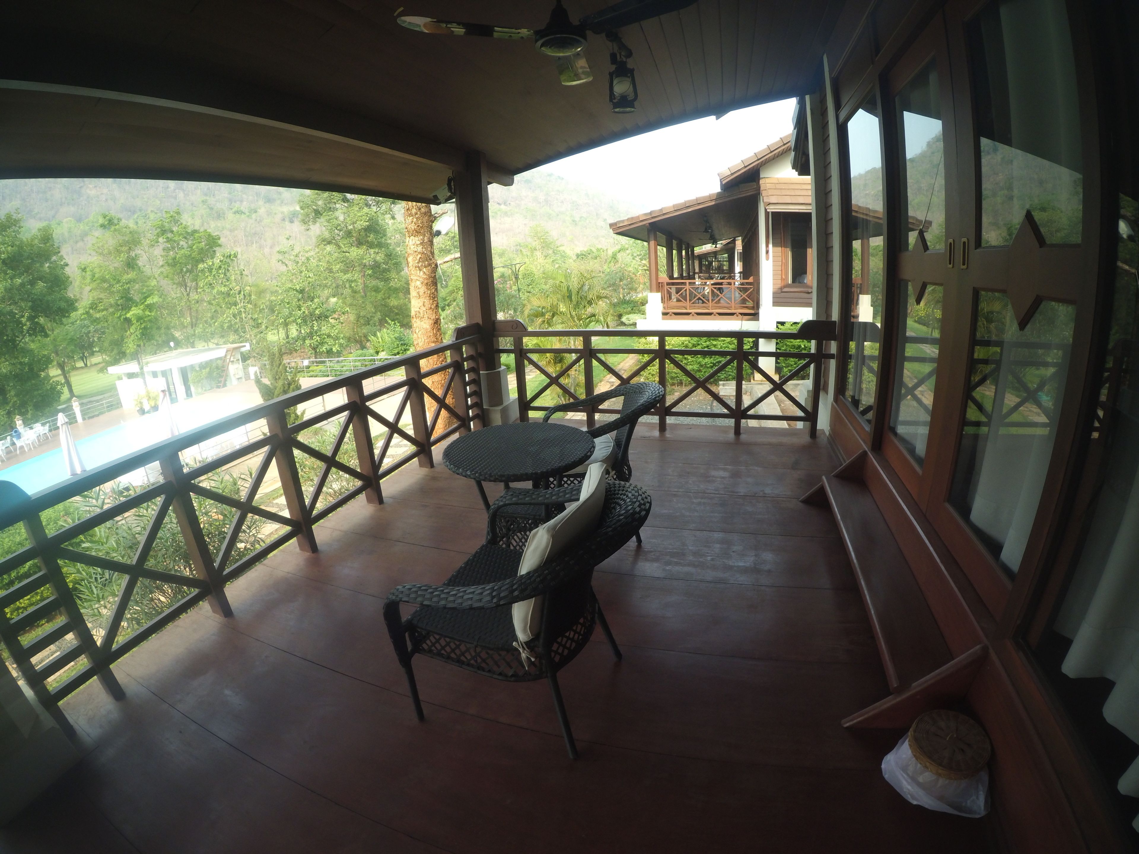 A wooden deck with a table and chairs, overlooking a swimming pool and lush greenery.