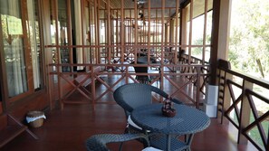Un espacio de estar al aire libre con techo, barandillas de madera, mesas y sillas.