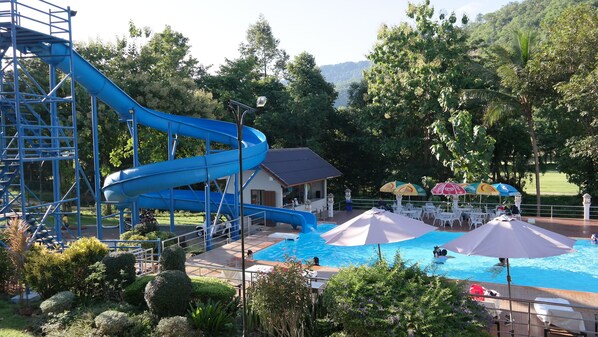 Parque acuático con un tobogán de agua azul, zona de piscina con sombrillas y un pequeño edificio.