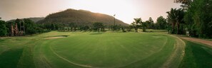 Ein Golfplatz mit einem großen, grünen Feld, Bäumen und einer Hügelkette im Hintergrund.