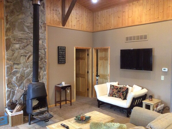 A cozy living room with a stone wall, a fireplace, a white sofa, and a television mounted on the wall.