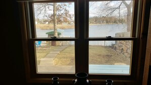 A window with a view of a lake, a tree, and a stone wall.