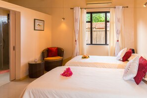 A hotel room with two beds, a wicker chair, a small table, and a window with curtains.