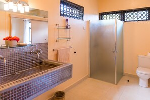 A bathroom with a tiled sink, a glass shower enclosure, a toilet, and a mirror with lights above.