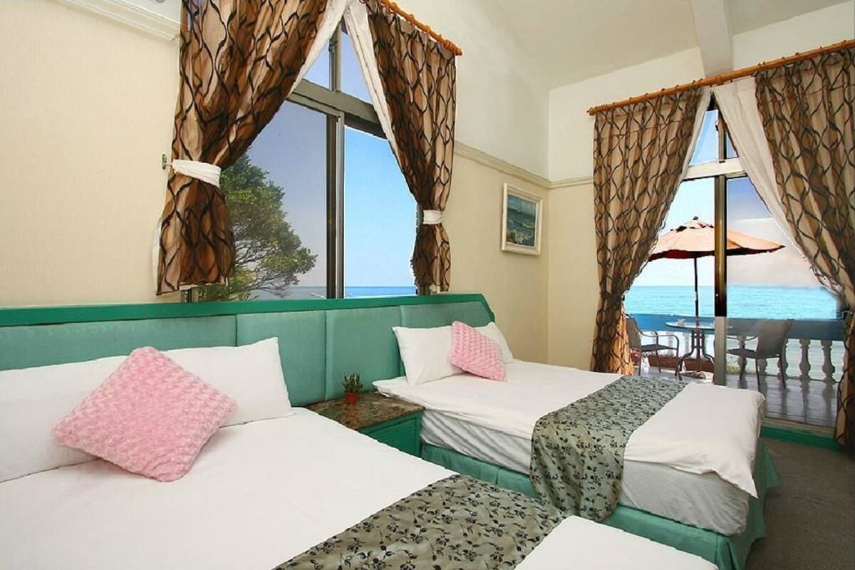 A hotel room with two beds, a view of the sea, and a balcony with an umbrella.