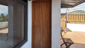 Une porte en bois portant le numéro 102, un mur recouvert de carreaux et une vue sur une terrasse en bois et une clôture.