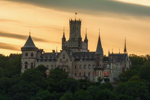 Un castillo grande e histórico con múltiples torres y una torre central destacada, rodeado de abundante vegetación.