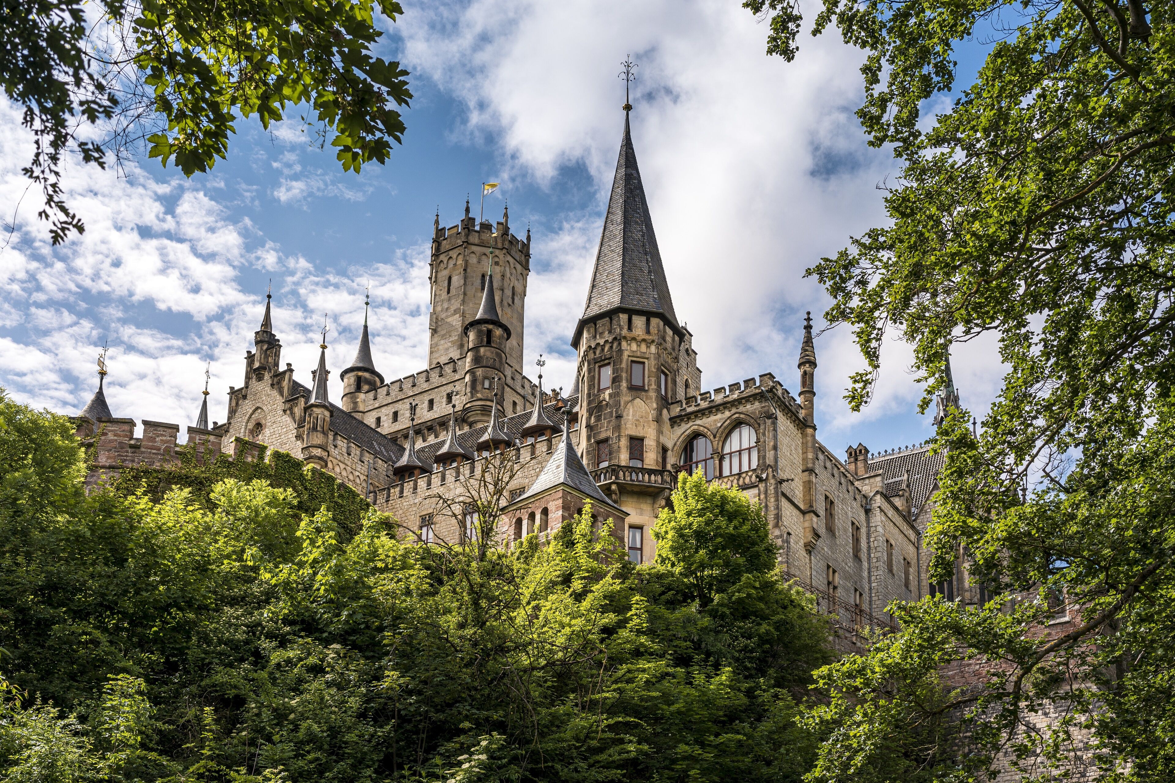 A historic castle with multiple towers and turrets, surrounded by lush greenery.