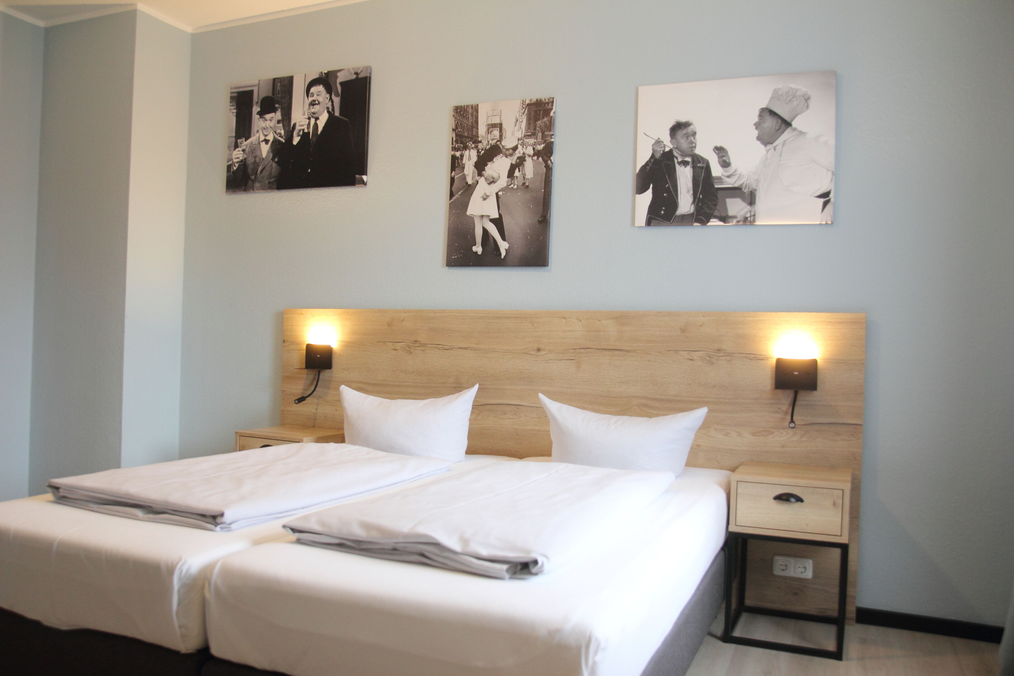 Habitación de hotel con una cama grande, dos mesitas de noche y tres fotografías blanco y negro en la pared.