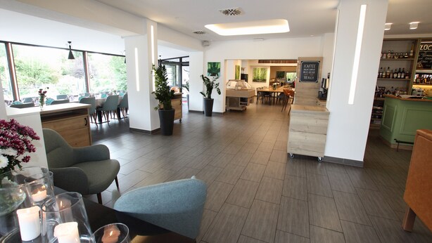 A modern interior with seating areas, a coffee bar, and a view of the outdoors. - zeitlos -  Hotel & Restaurant am Fuchsbach (Pattensen)