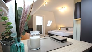 A modern hotel room with a wooden desk, a vase with dried plants, a candle, and a bedside table with a lamp. - zeitlos -  Hotel & Restaurant am Fuchsbach (Pattensen)
