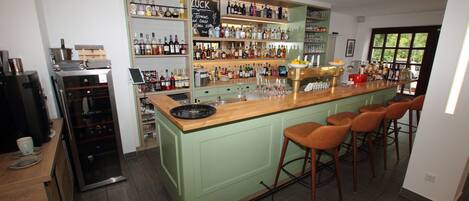 A bar area with a green bar counter, multiple stools, and shelves stocked with bottles and glasses.