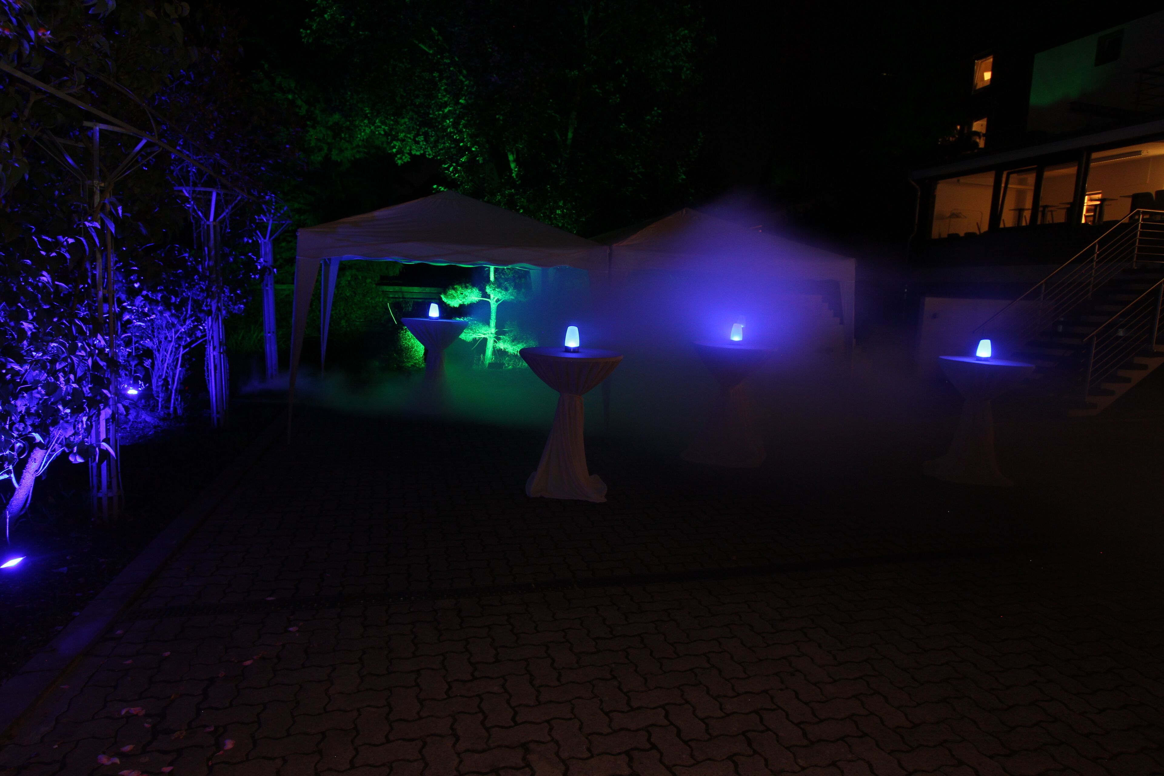 Un espacio al aire libre con carpas, una fuente e iluminación ambiental.