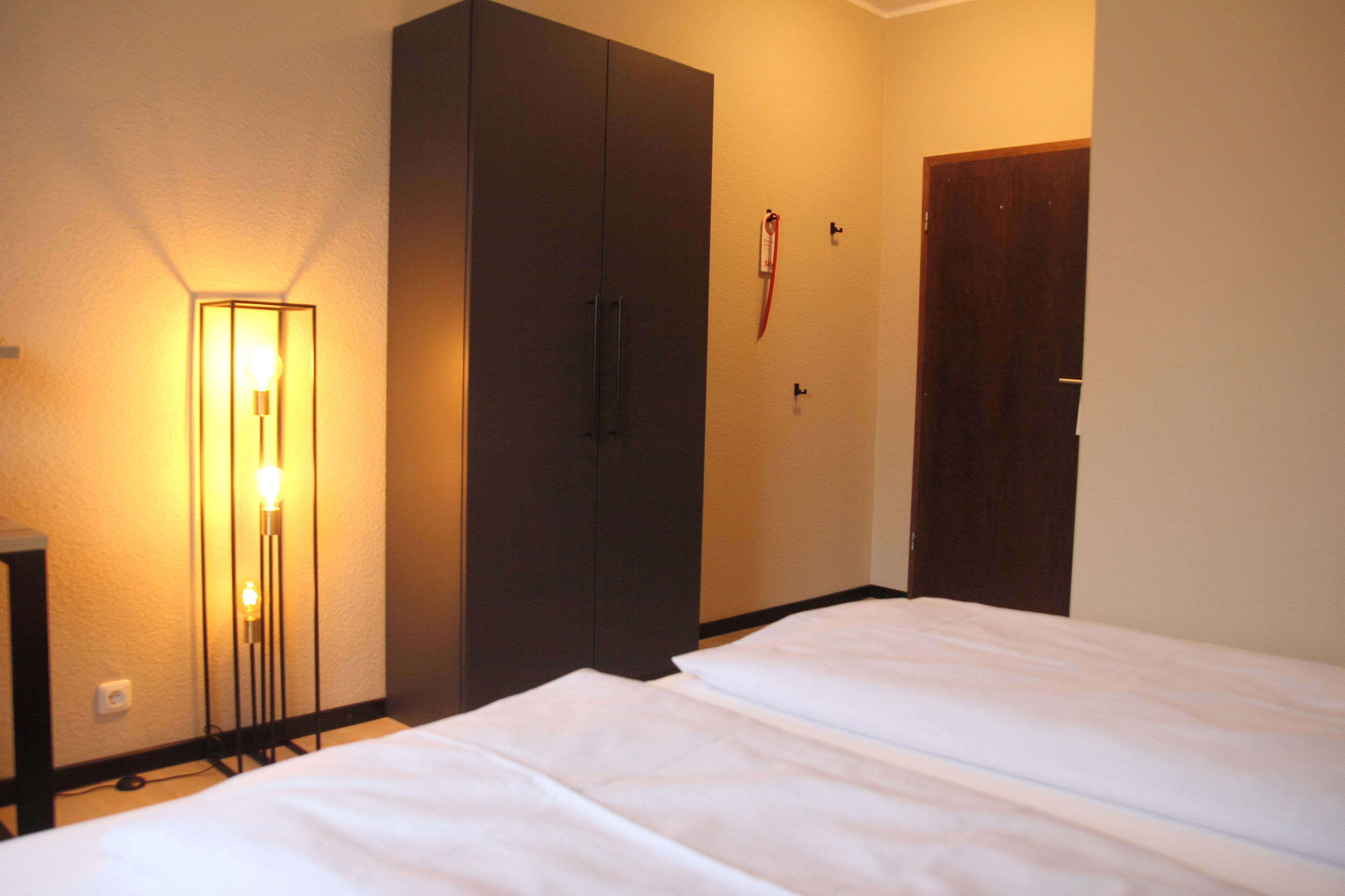 Quarto de hotel com duas camas, um guarda-roupa, um abajur e uma porta.