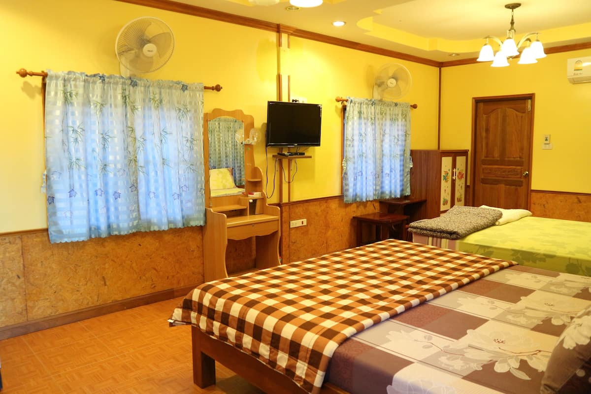 A hotel room with a bed, a desk, a chair, a television, and two wall fans.