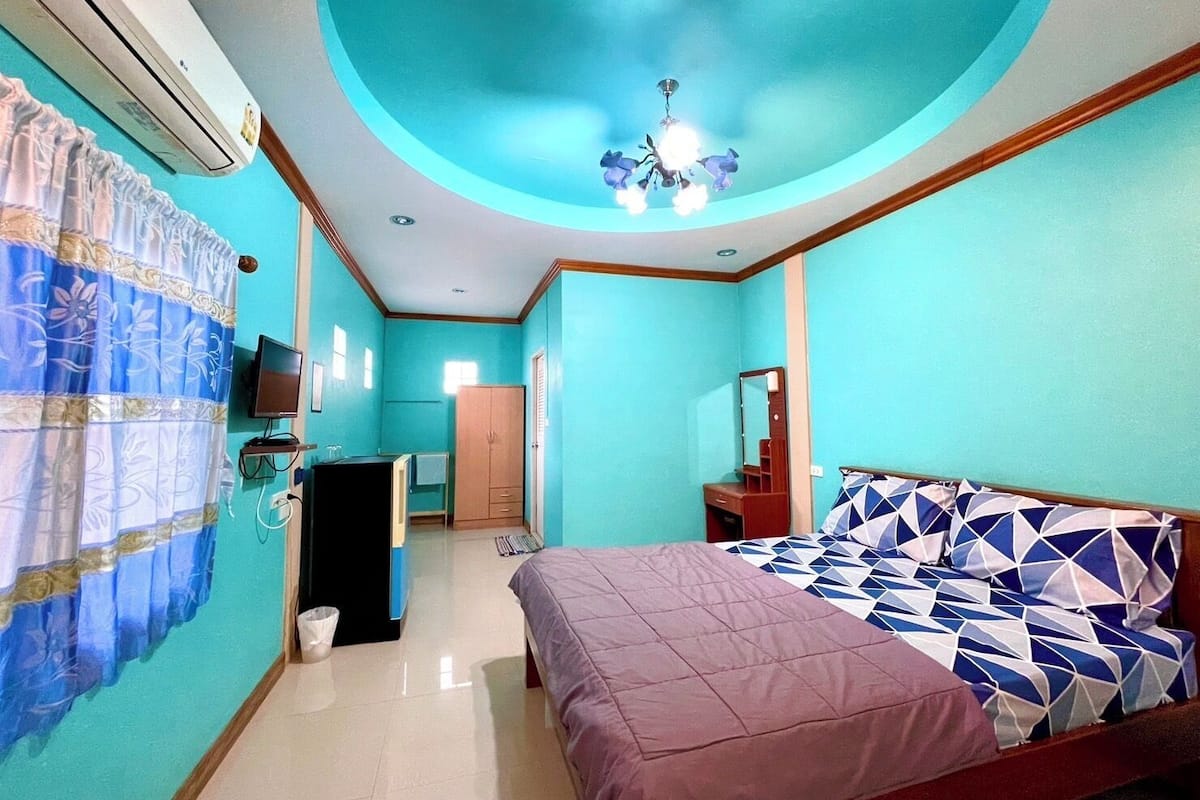 A bedroom with a bed, a dresser, a mirror, a ceiling fan, and an air conditioning unit.