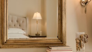 A mirror with a gold frame, a bedside lamp, and a stack of books on a mantelpiece. - Noble Suites (Athens)