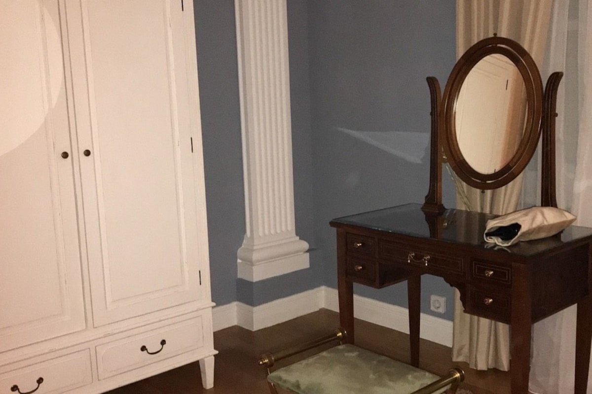 Una habitación con un armario blanco, una tocador de madera con espejo y una silla verde.