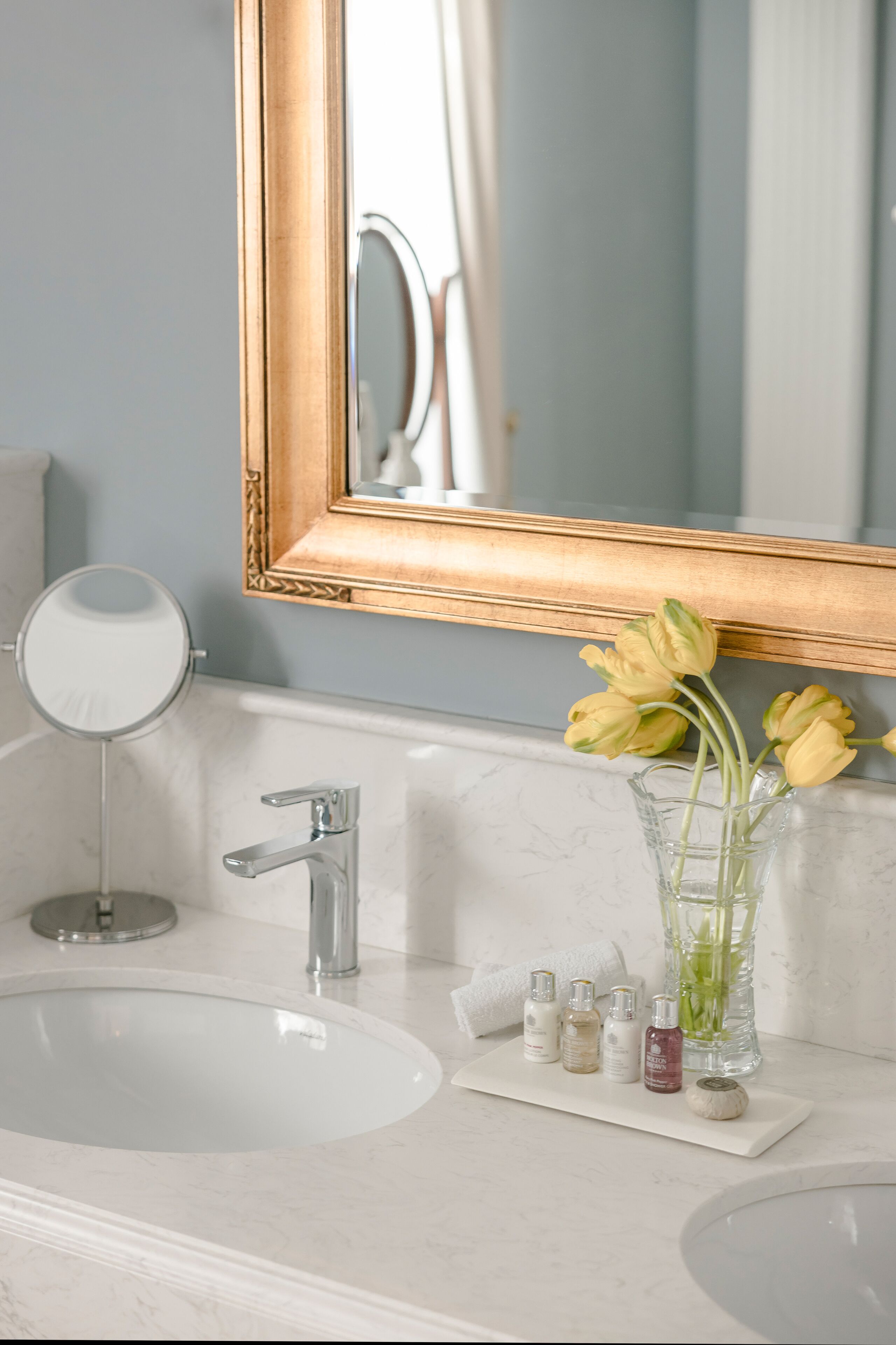 Un baño con lavamanos blanco, un espejo y un florero con flores.