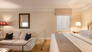 A hotel room with a bed, a sofa, a mirror, a window with curtains, and a lamp.