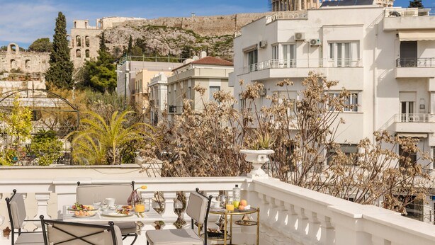 A terrace with tables and chairs, overlooking a cityscape with historical buildings and a hill. - Noble Suites (Athens)