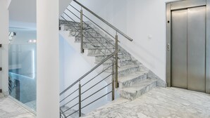 Un intérieur moderne avec un escalier en marbre, un ascenseur en verre et une rambarde en métal.