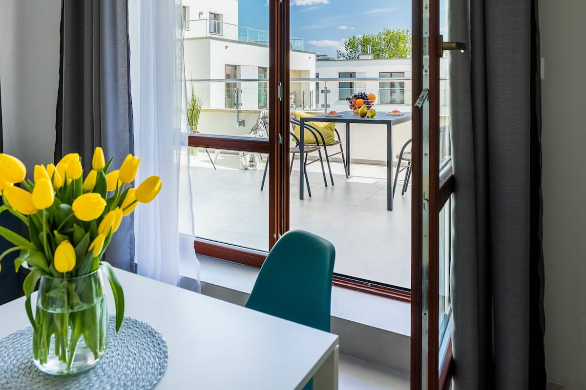 Une pièce avec vue sur un balcon, une table à manger ornée d’un vase de tulipes jaunes et un canapé bleu.