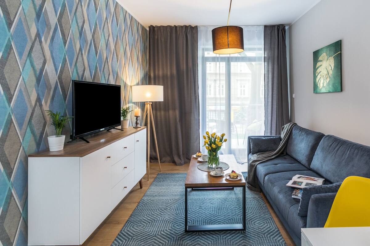 Un salon moderne doté d’un téléviseur, d’un canapé, d’une table basse et offrant une vue sur la ville grâce à de grandes fenêtres.
