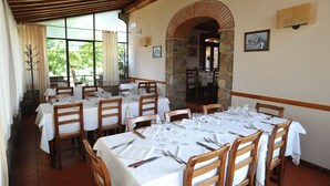 A restaurant with multiple tables set for dining, featuring stone arches and wooden beams. - Hotel Restaurant La Torricella (Poppi)