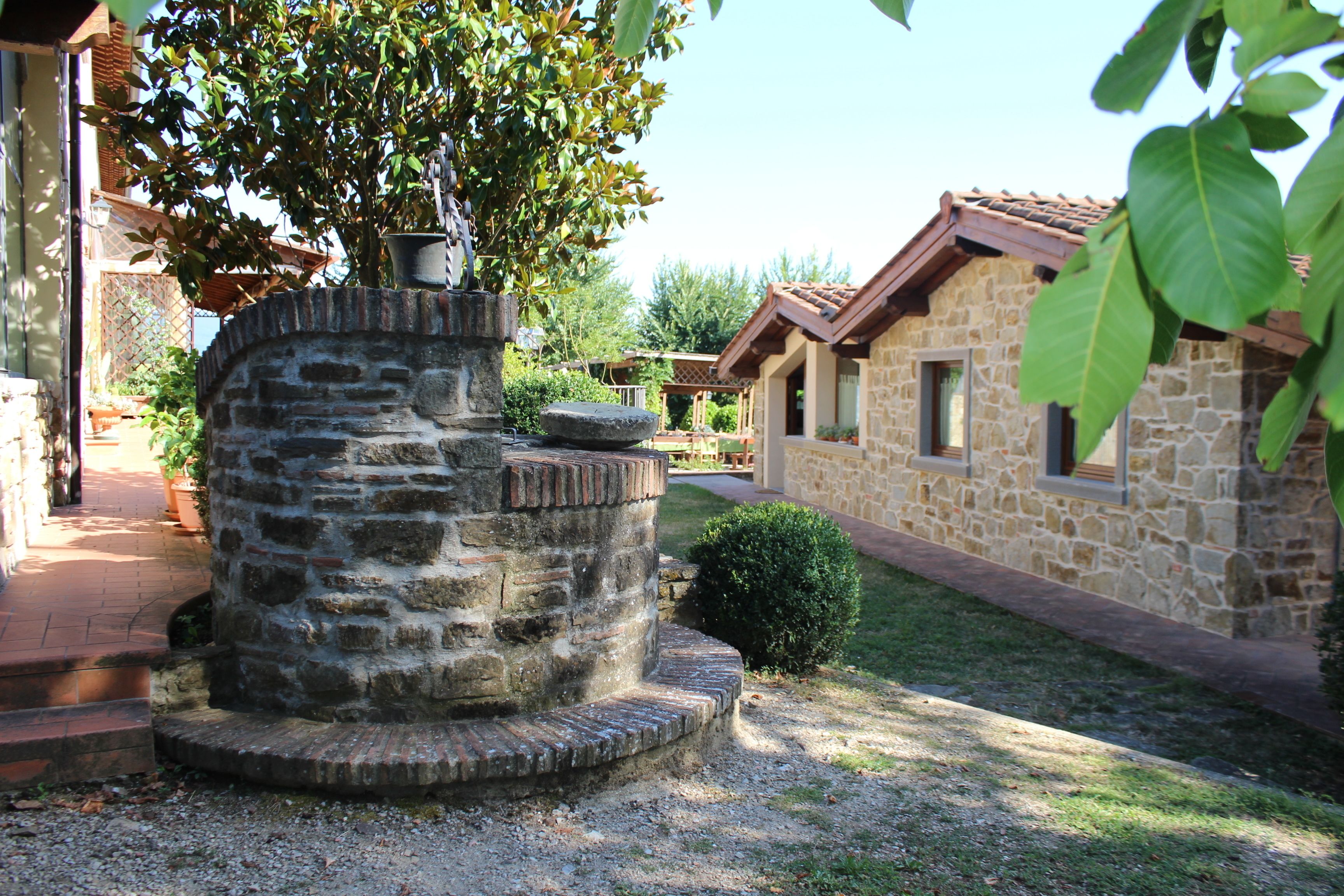A stone well with steps, surrounded by a garden with a stone building in the background.