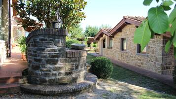 A stone well with steps, surrounded by a garden with a stone building in the background.
