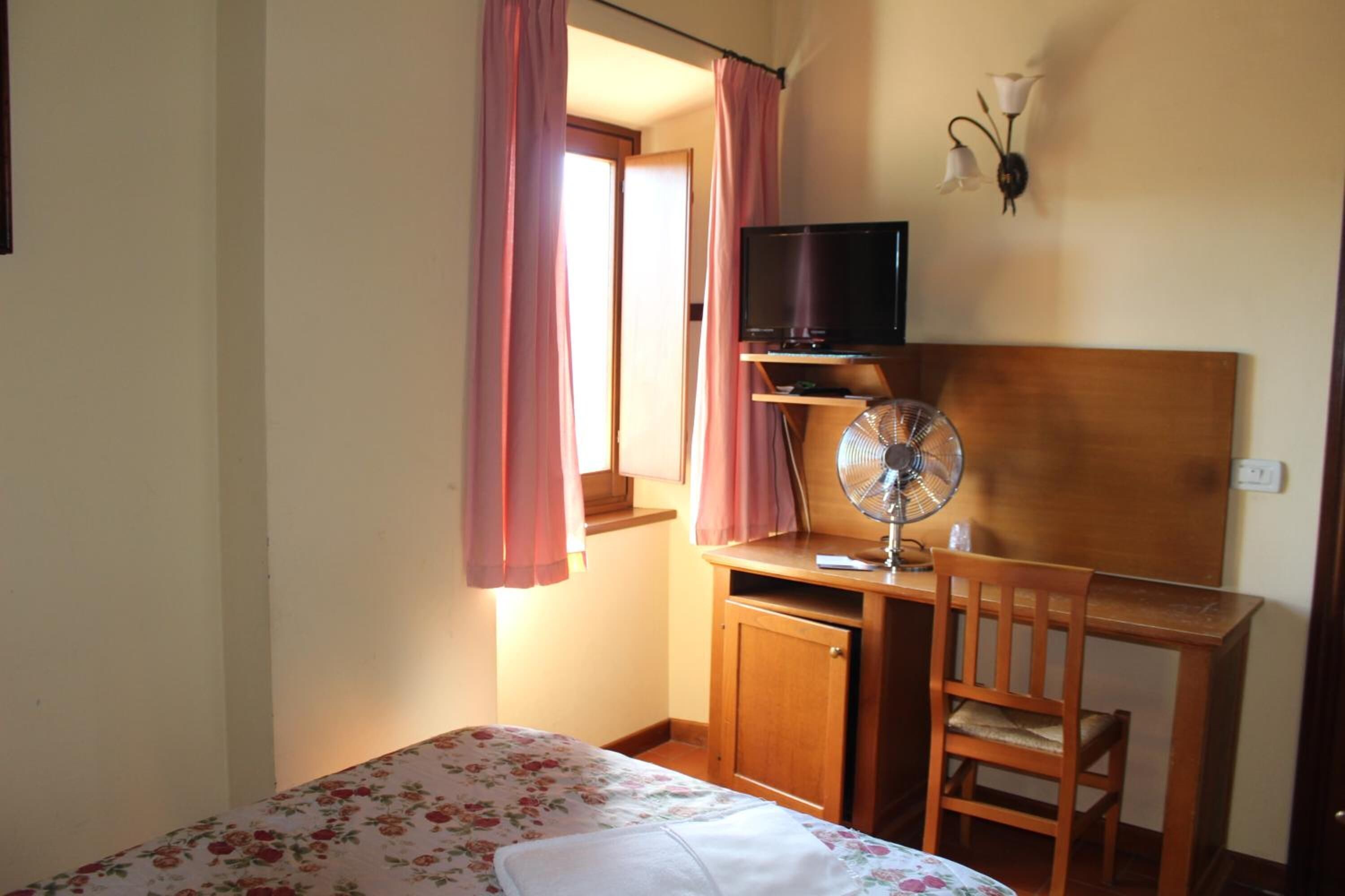 Ein Schlafzimmer mit Bett, Schreibtisch, Stuhl, Fernseher und Ventilator.