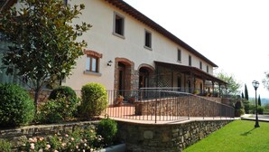 A two-story building with a stone facade, a covered patio with a metal railing, and a well-maintained garden with roses. - Hotel Restaurant La Torricella (Poppi)