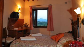 A bedroom with a wooden ceiling, a bed with floral bedding, a desk with a lamp, and a window with a view.