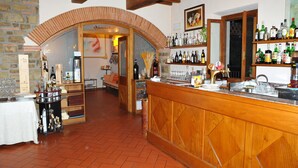 A bar area with a wooden counter, shelves with bottles, and a stone wall. - Hotel Restaurant La Torricella (Poppi)