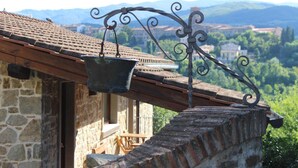 A stone building with a metal bucket hanging from a curved metal bracket. - Hotel Restaurant La Torricella (Poppi)