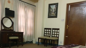 A bedroom with a bed, a desk, a chair, a television, and a door. - Om Pension Guest House (Lalitpur)