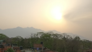 A residential area with houses and trees, a mountain range in the background, and the sun low on the horizon. - Om Pension Guest House (Lalitpur)