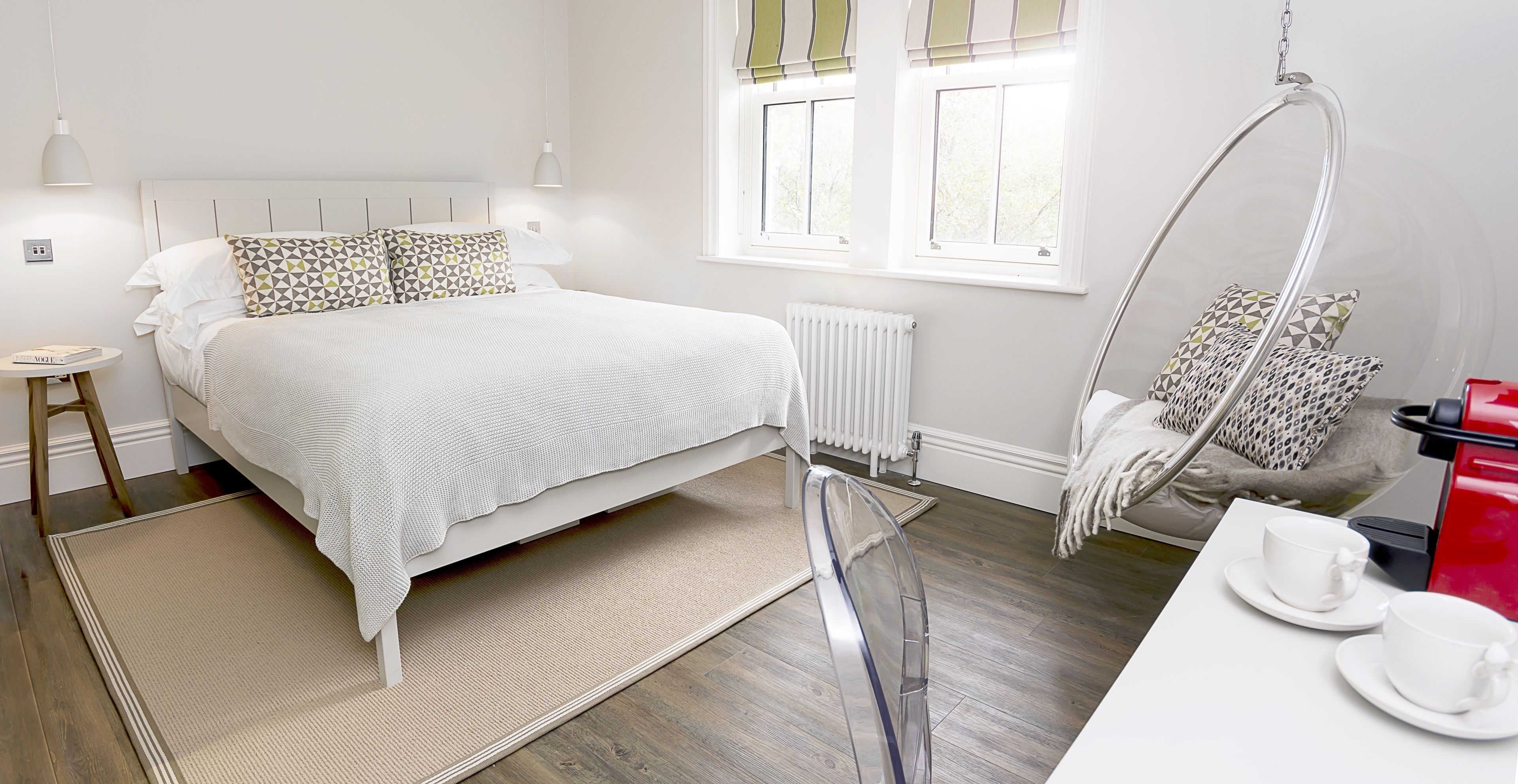 A modern bedroom with a large bed, bedside tables, a hanging chair, and a coffee machine.