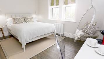 A modern bedroom with a large bed, bedside tables, a hanging chair, and a coffee machine.
