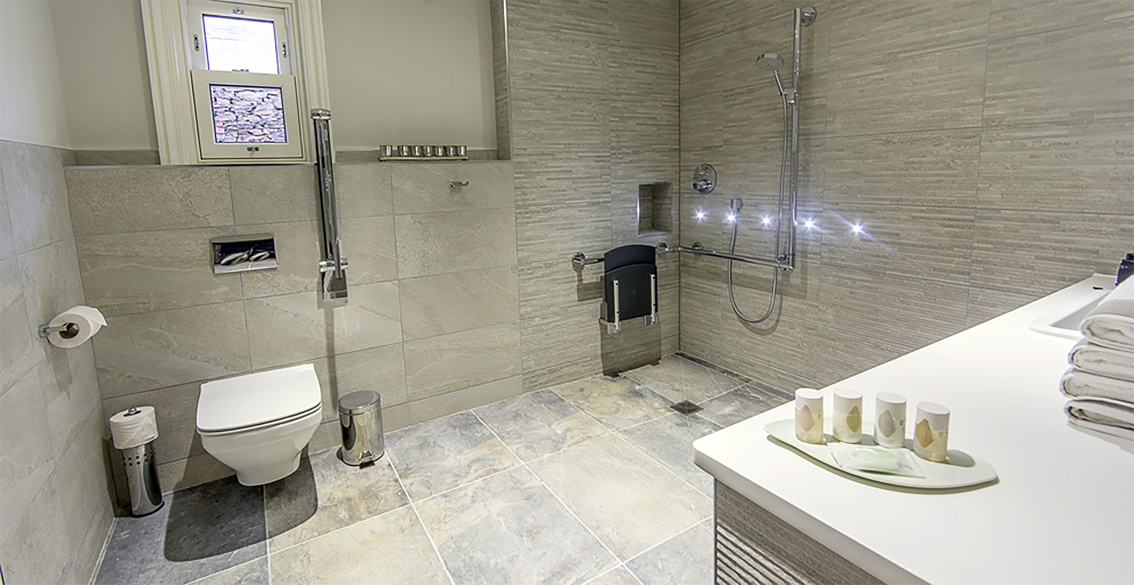 A modern bathroom with a toilet, bidet, and shower. There is a sink with towels and a small trash can.