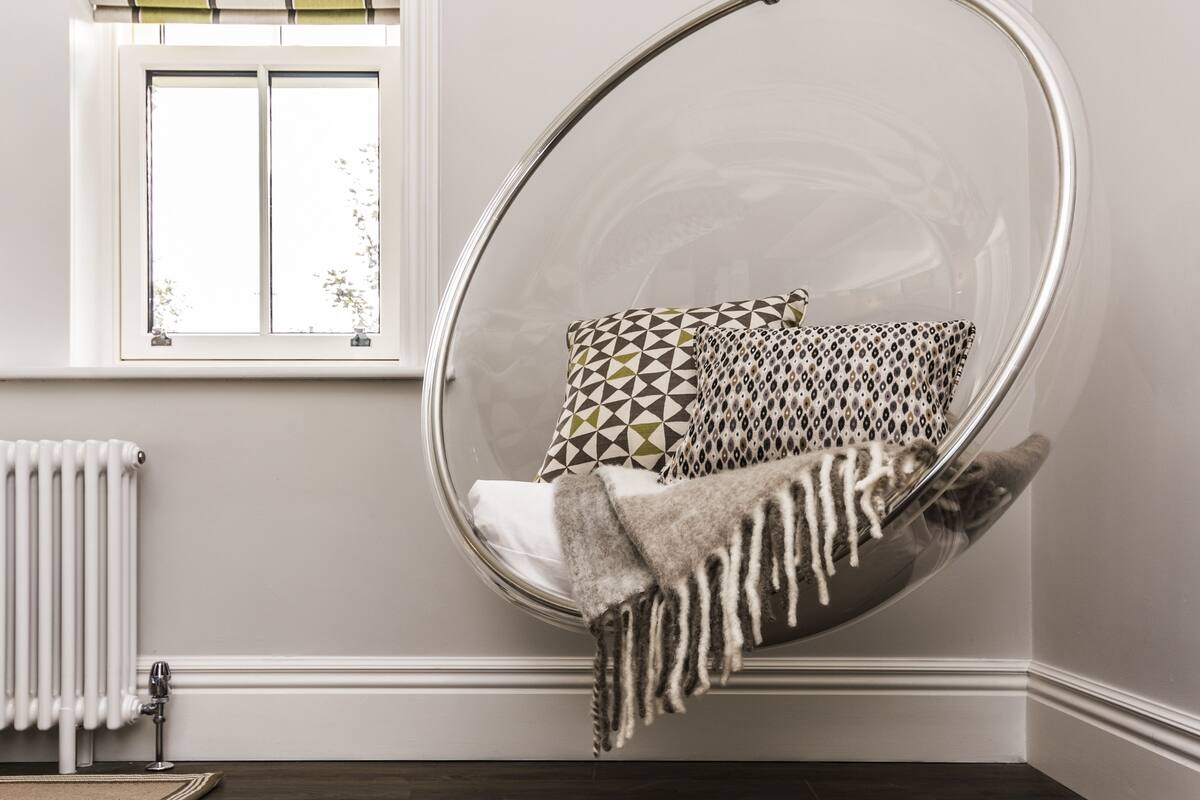 Quarto com uma cadeira suspensa, um radiador, uma janela com persianas e uma almofada estampada.