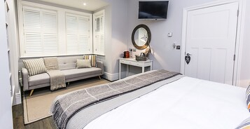 Un dormitorio con una cama, una mesita de noche con espejo, un sofá y un televisor montado en la pared.