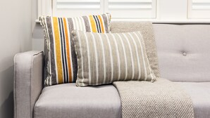 Un sofá gris con dos almohadas a rayas y una manta de diseño geométrico.