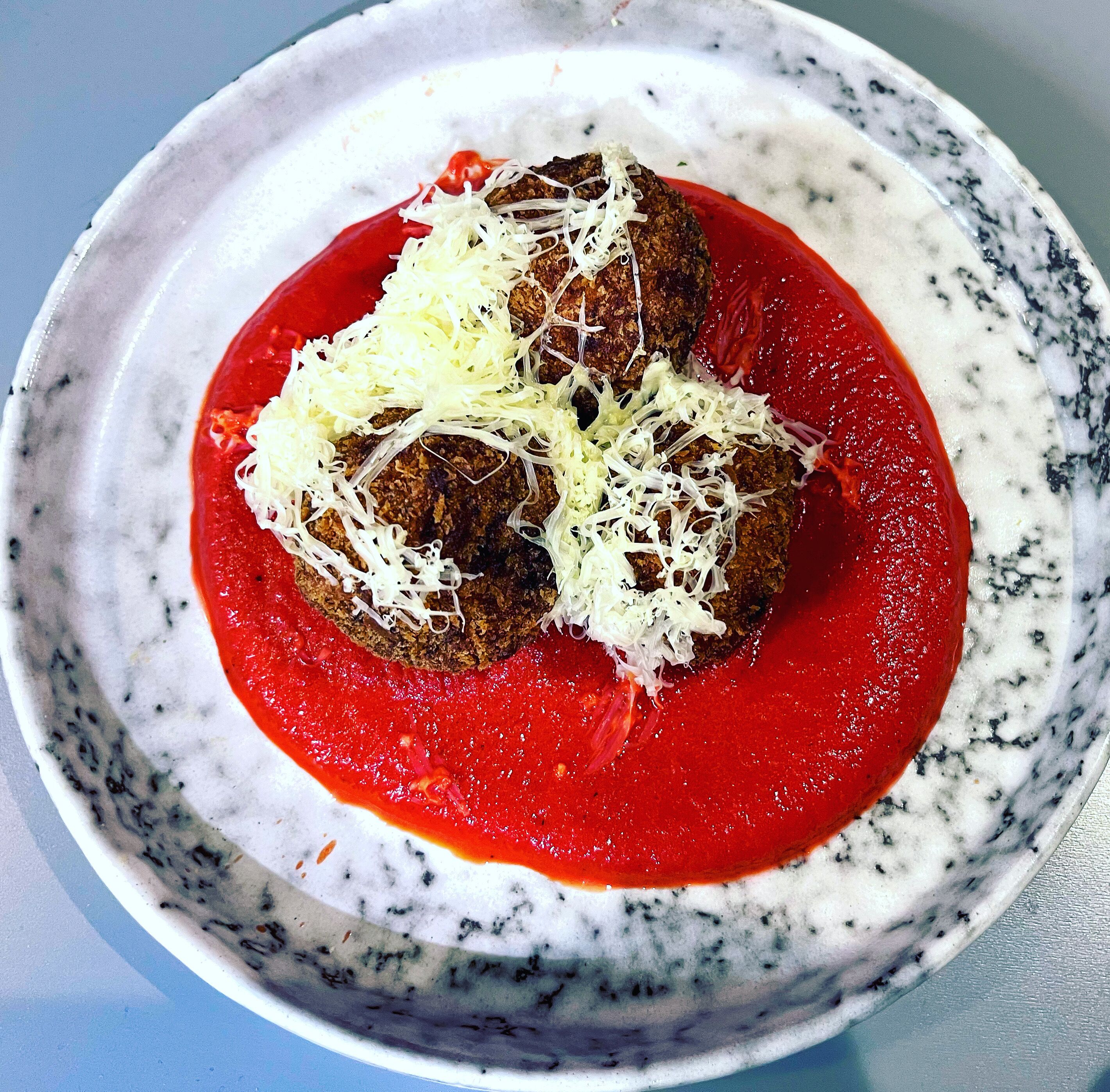 A bowl of meatballs with tomato sauce and shredded cheese.