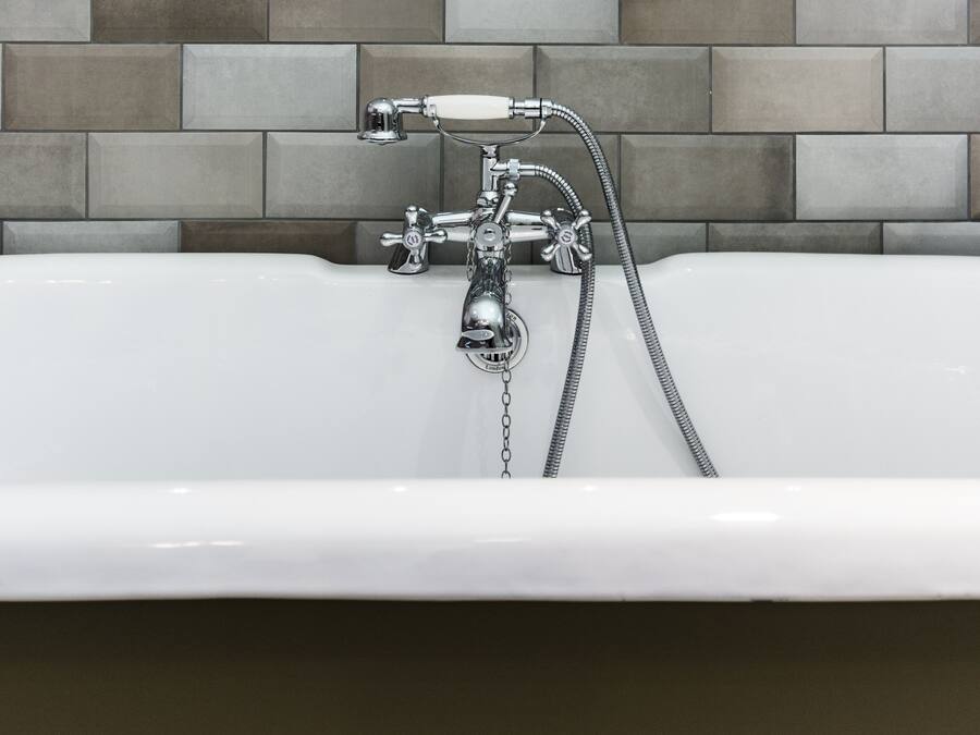 A modern bathroom with a chrome faucet and shower head, a white sink, and a tiled wall.