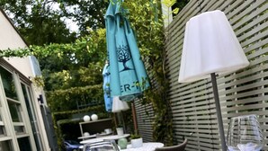 Un espacio de comedor al aire libre con mesas dispuestas para una comida, incluyendo platos de comida, cubiertos y una copa de vino.