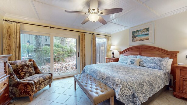Ein Schlafzimmer mit einem großen Bett, einem hölzernen Kopfteil, einer Bank, einem Stuhl, einem Nachttisch und einem Deckenventilator.